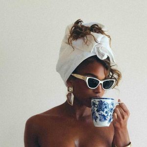 Glamorous woman with a towel wrap and sunglasses sipping tea, post-shower skincare aesthetic, spray tan prep, luxury self-care vibes.