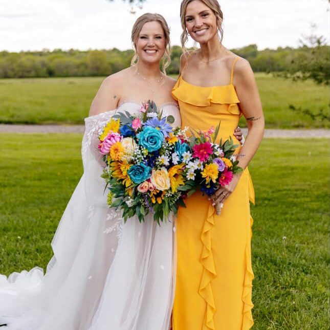 Bride and bridesmaid with flawless Sunny Daze Sunless spray tans outdoors holding wedding bouquets in Kansas