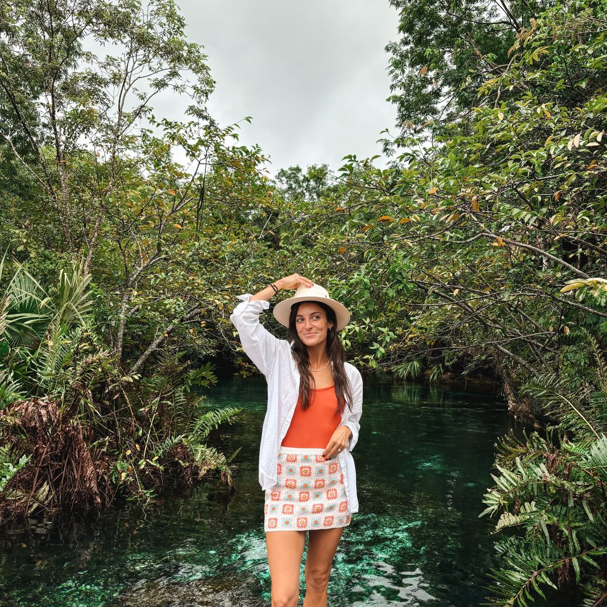 Tanned woman in a breezy vacation outfit with a hat, enjoying a tropical getaway
